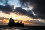 An ocean tanker under dark clouds and sunlit vapour trails