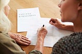 younger woman helping senior woman sign her last will and testament