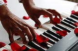 Brown hands playing a keyboard with rose petals scattered over it