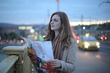 woman holding a map stands on a highway looking out at something in the distance