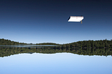 Upside-down image of a blue lake above a blue sky with a white raft seeming to hover in the sky.