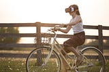 Girl with flowery skirt on a bike in a bucolic setting, wearing a virtual reality headset