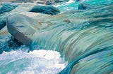 Close up shot of blue turquoise blue water flowing over smooth rocks