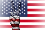 A hand holding up a peace sign with an American Flag image laid over it