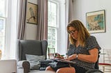 Woman reviewing bills and paperwork at home while making notes, reflecting careful budgeting and financial planning. Photo by Centre for Ageing Better on Unsplash