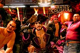 Pirate captain Goro Majima and his crew pose for a celebratory moment, group-photo style. A “Pirates Coliseum” sign hangs in the background alongside some dramatic lights.