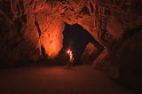 Man lifts up a red flare light inside a cave.