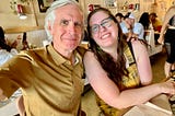 And older man and his 20-something daughter dressed in yellow sit in a cafe