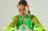 Woman in a bright green outfit staring into a crystal ball.