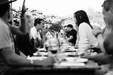 People sitting at a long dinner table outside, engaging each other in conversation