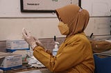 Woman wearing PPE handling vaccine.