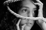 portrait of a girl with with loose coils of rope over her head and hands near her face