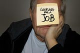 Man with a post it on is forehead which reads “looking for a job”