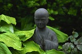 There is a statue of a mediating monk carved in stone in between leaves.