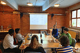 A group of the Energise Manchester team members sitting around a table looking at a presentation screen. Ellie Kuitunen is presenting.