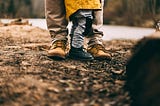 Image of little person standing beside parent, view of shin level down to their shoes.