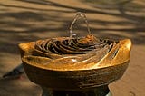 A beautiful stone crafted faucet with water flowing from what looks like a bud, nipple or hill-like protrusion. It is seemingly hand carved with a rose pattern.