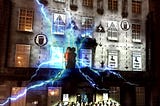 Image from Imitating the Dog’s piece Trespass. A choir of people are in front of a building with vibrant projection on it. The central projected image is of a person a the heart of lightning bolts.