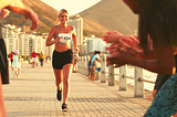 Female runner crossing race finish line in last place, friends are cheering, she is smiling.