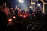 Students and faculty in front of the arch at Washington Square Park at night, holding candles.