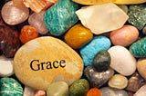 Image of many colorful smooth rocks and one larger yellow one with the word grace on it.