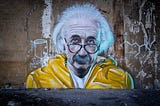 A graffiti portrait of Albert Einstein in a yellow hoodie, with glasses.