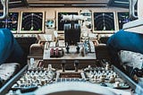 A plane dashboard with lots of buttons and levers, and a pilot and copilot