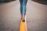 A woman walking a yellow line on a highway