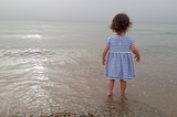 A young girl in blue-white striped dress standing in the shallow waters.