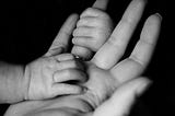 Black and white photo of baby gripping mother’s finger