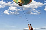 A beautiful blue sky with puffy white clouds, a colorful hot air balloon is at the top and upside down legs at the bottom, connected to the balloon with a very thin bungee cord, showing someone jumped off the hot air balloon.