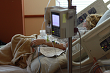 woman on her side in a hospital bed attached to machines and drips