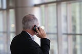 A grey-haired man in a suit talks on telephone.