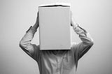 A black and white photo of a man with a box over his head.