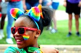 Young girl of colour at a pride parade wearing rainbow accessories and smiling