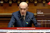 A bald man in a dark blue suit and tie is speaking at a podium in a formal government setting. He has a serious expression and is flanked by two microphones. A small pin with the colors of the Ukrainian flag is attached to his suit lapel. The background is ornate wooden paneling. The overlay text identifies him as Claude Malhuret, a senator from Allier and president of the political group Les Indépendants.