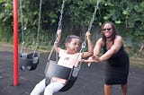 Child on a swing being pushed by a smiling woman, showing patience and right timing.