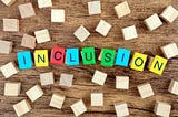 An image of the word inclusion spelled out on a table with different color blocks surrounded by wooden blocks