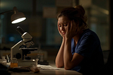 A weary medical laboratory scientist, sitting quietly beside a microscope under dim light, capturing the silent emotional weight of burnout and exhaustion.