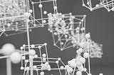 The image depicts a three-dimensional molecular structure model. It consists of interconnected spheres and rods, representing atoms and bonds, respectively. The spheres are likely to symbolize different atoms, while the rods illustrate the chemical bonds between them. The structure appears complex, with multiple layers and connections, suggesting a detailed representation of a molecular or crystalline lattice. The grayscale color scheme emphasizes the geometric and spatial relationships.
