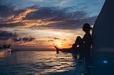 an image of a woman sitting on shallow body of water during sunset.