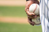Pitcher holding two baseballs by his side.