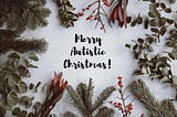 Christmas background — pine, eucalyptus, berries — with black text in the centre that reads Merry Autistic Christmas!