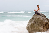 woman sitting peacefully on a large rock surrounded by ocean waves