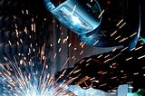 A person in protective gear welding a metal bar.