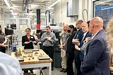 A group of people observe a manufacturing demonstration in a university lab.