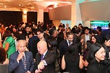 A crowd of people having drinks and in conversation in the lobby outside the main gala room. The crowd is very diverse and inclusive, with young and older adults, women and men, from the broadest definition of the Asian diaspora and non-Asian friends and family.