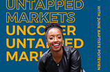 A Black woman is sitting and smiling wearing a black leather jacket with blue jeans in front of a navy blue background with the podcast title juxtaposed one on top of the other. It says Uncover Untapped Markets in bold yellow at the top and regular yellow font at the bottom. On the right-hand side it says with Junie Baptiste Poitevien, who is the podcast host.