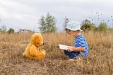 A child reading a story to her stuffed bear.