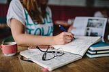 Long haired woman sitting at a desk writing in a notebook